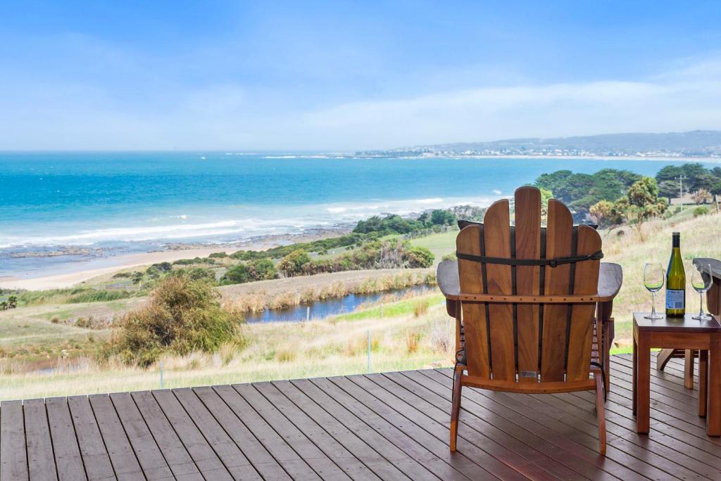 a wooden deck with a chair and a table with wine bottles at Seafarers Getaway in Apollo Bay