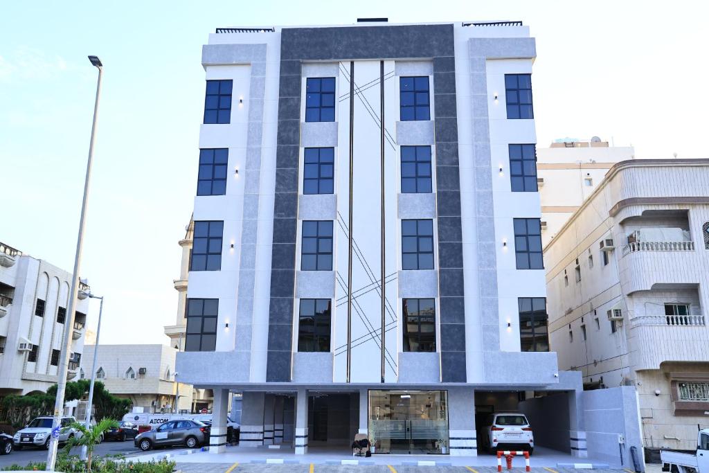 a tall white building with cars parked in a parking lot at شقق فندقية للضيافة - تتم ادارته من قبل مضيف مستقل - Hotel apartments for private hospitality in Jeddah