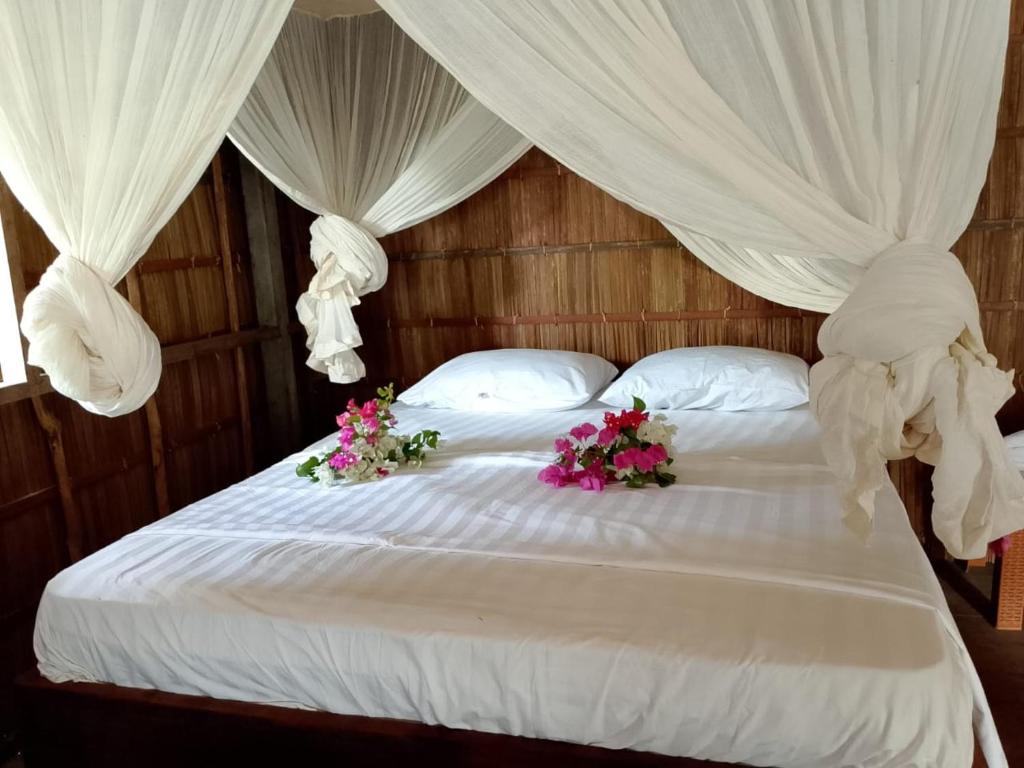 łóżko z białymi zasłonami i kwiatami w obiekcie Black Coral Raja Ampat Homestay w mieście Poelau Mansoear