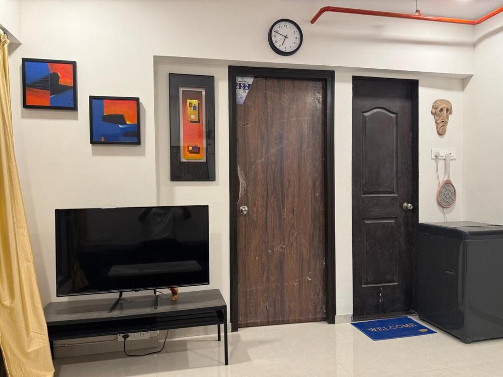 a living room with a tv and a door and a clock at Creek View Studio Apartment in Mumbai