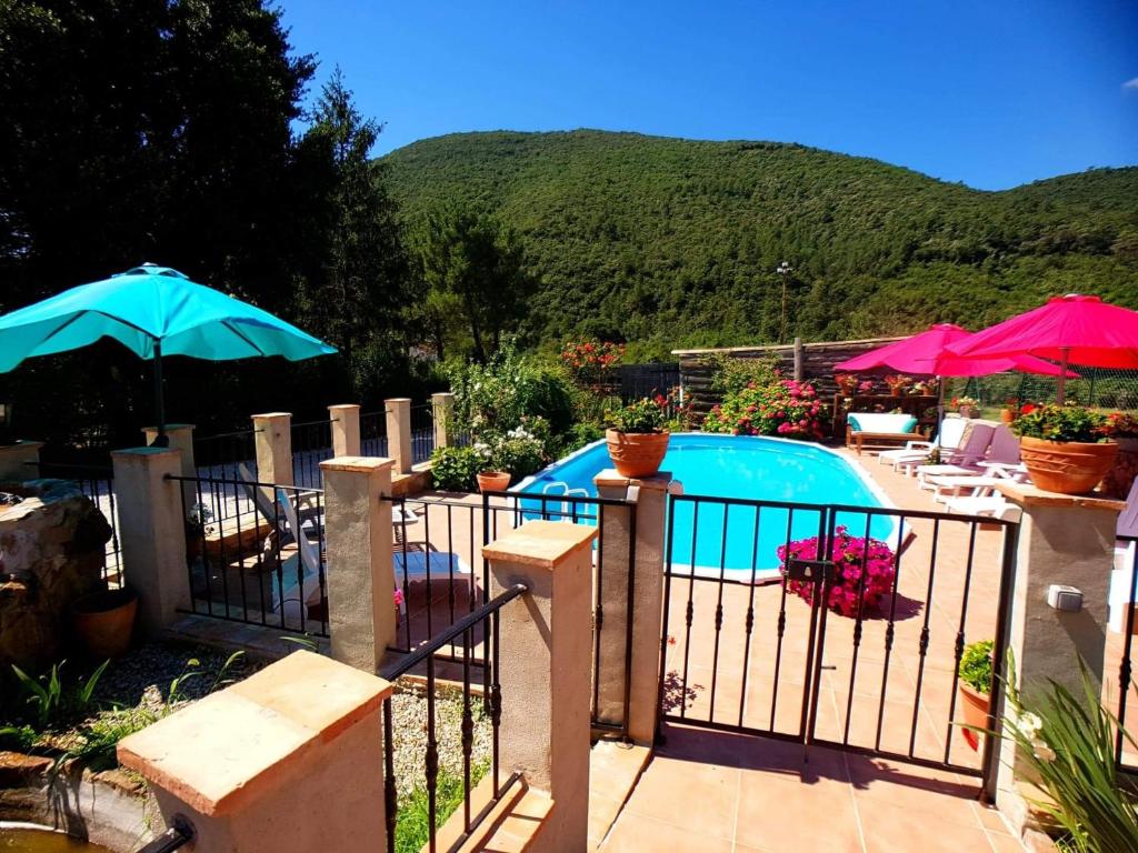 une clôture avec une piscine et des parasols dans une cour dans l'établissement Le Mas Joyeux - Gîte L'Orchidée en Cévennes, à Saint-Florent-sur-Auzonnet