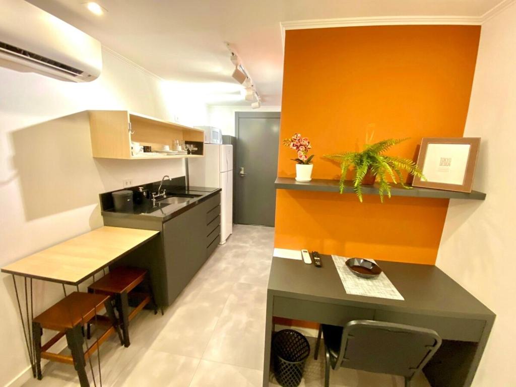 a kitchen with an orange wall and a black counter at Estudio no Centro de Curitiba in Curitiba