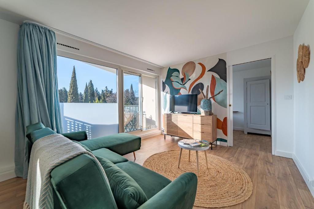 - un salon avec un canapé vert et une grande fenêtre dans l'établissement Fables du Jardin de la Fontaine, à Nîmes