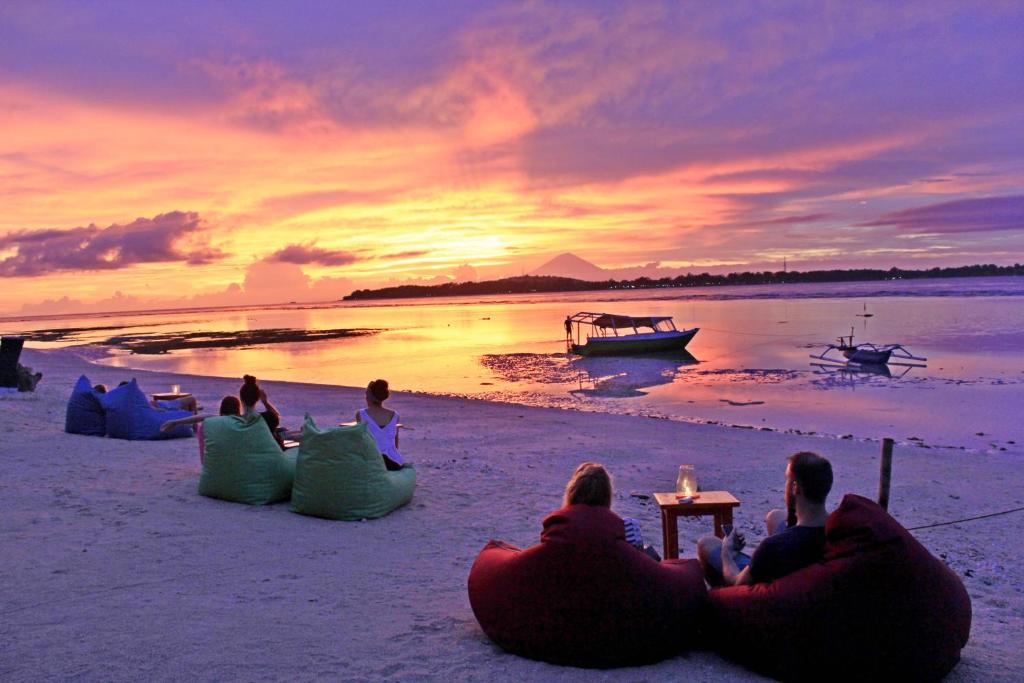 a group of people sitting on the beach watching the sunset at Pandan Bungalow in Gili Air