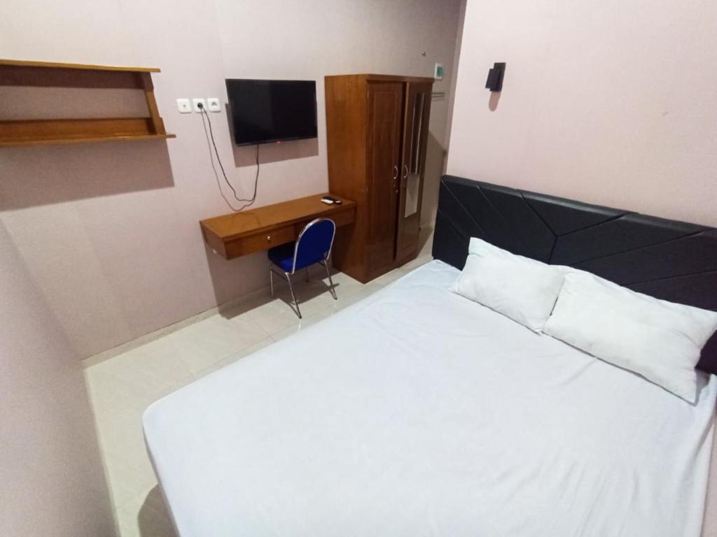 a bedroom with a bed and a desk and a television at De Corner 2 Madiun RedPartner in Madiun