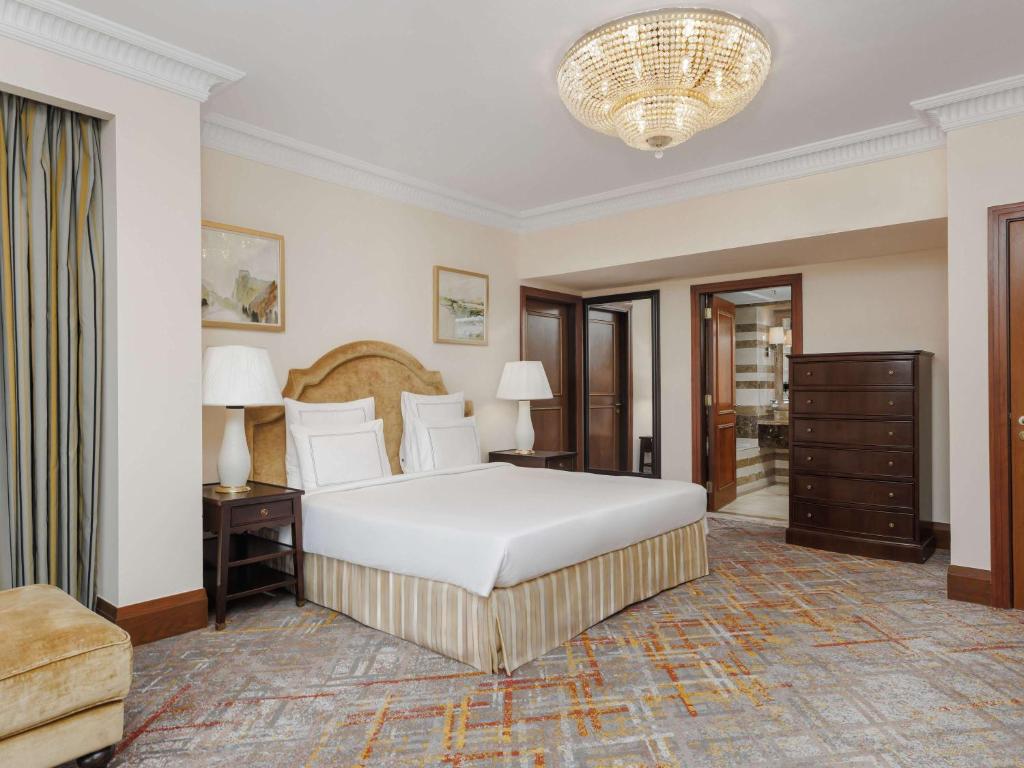 a bedroom with a large white bed and a chandelier at Swissotel Al Maqam Makkah in Mecca