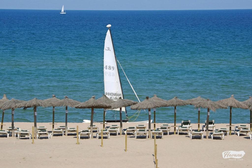 ein Segelboot am Strand mit Stühlen und Sonnenschirmen in der Unterkunft Casa adosada en Platja de Pals by Apartaments Golf in Pals