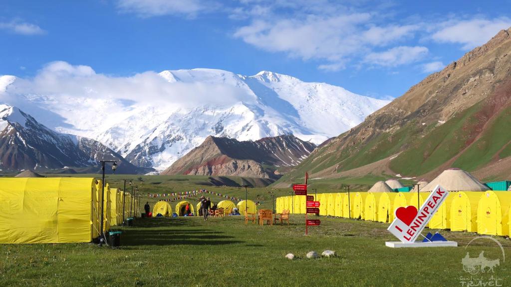 a group of yellow tents in a field with mountains at Yurt Glamping Edelweiss Meadow at the foot of Lenin Peak in Sary-Mogul