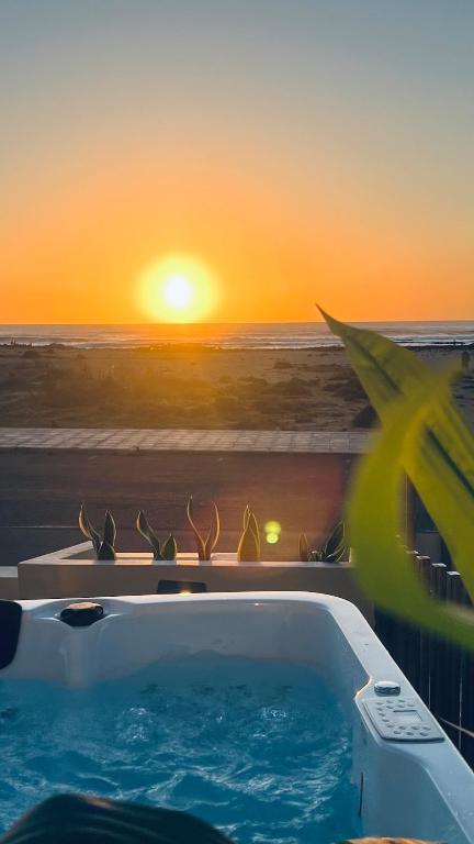 a hot tub with a view of the ocean at sunset at Amber Skies Seafront Retreat in El Cotillo