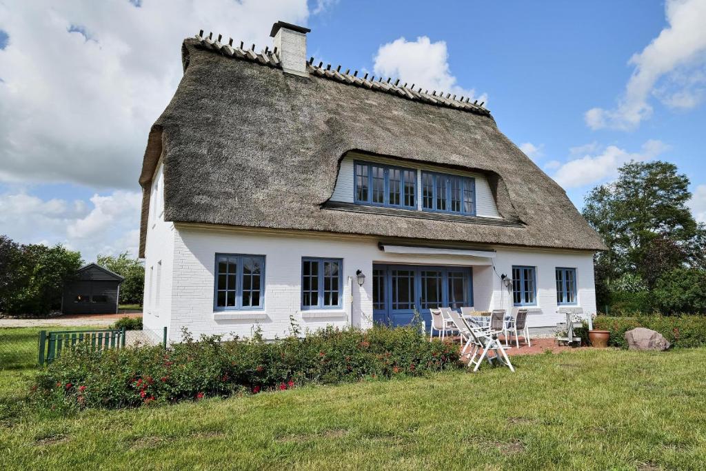 a white house with a thatched roof on a field at Landhaus Markerup in Husby