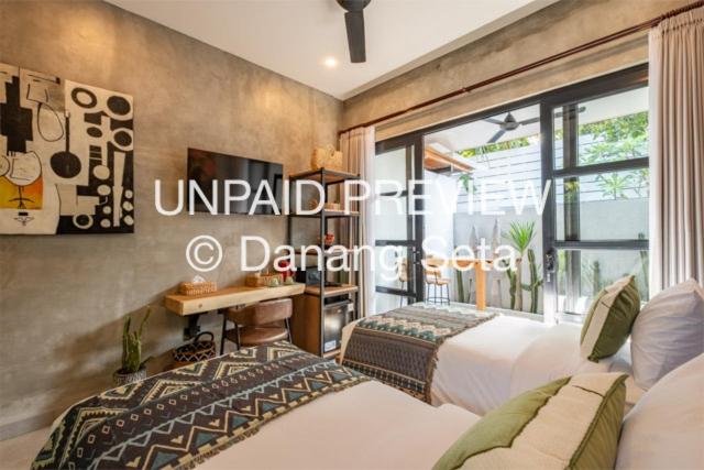 a bedroom with two beds and a desk and a window at Lila Nest in Ubud