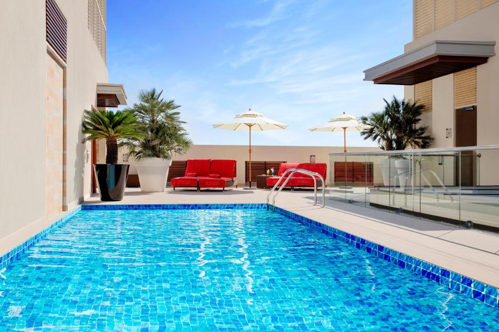 a pool with chairs and umbrellas on a building at Centro Capital Doha - By Rotana in Doha