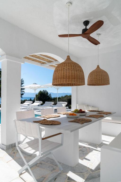 a white dining room with a table and a ceiling fan at Villa Seascape, Beachfront Living in the Greek Riviera Porto Heli in Porto Heli