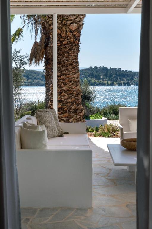 a white couch sitting on a patio with a palm tree at Villa Seascape, Beachfront Living in the Greek Riviera Porto Heli in Porto Heli