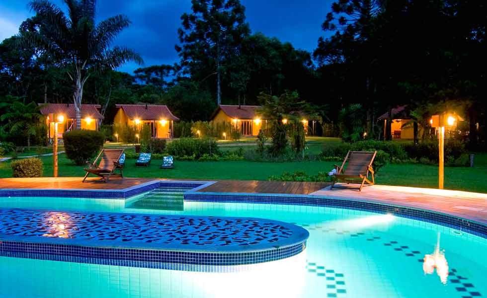 a swimming pool with two chairs and a yard at night at Pousada Villa Acauã in Visconde De Maua