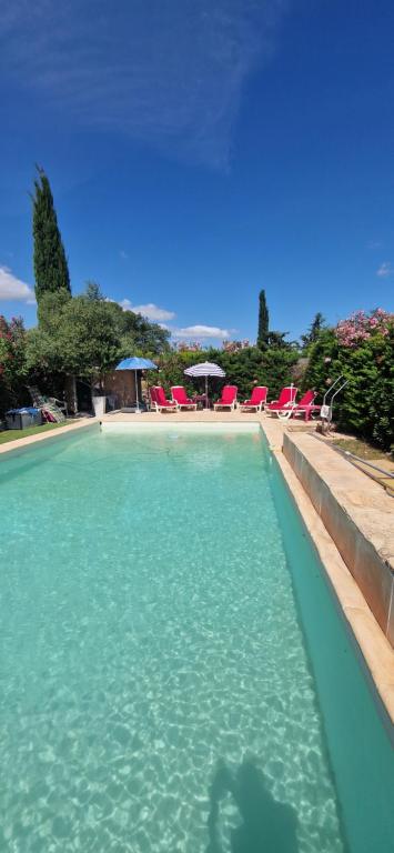 une piscine d'eau bleue avec des chaises rouges et des parasols dans l'établissement Maison dans les vignes, aux Arcs-sur-Argens