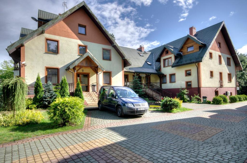 Large house with multiple gables, parked car, and landscaped garden under a blue sky.