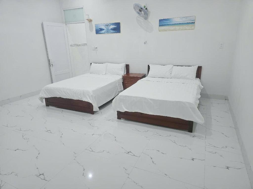 two beds in a white room with marble floors at Nhà Khách Hoàng Thắng in Bồng Sơn