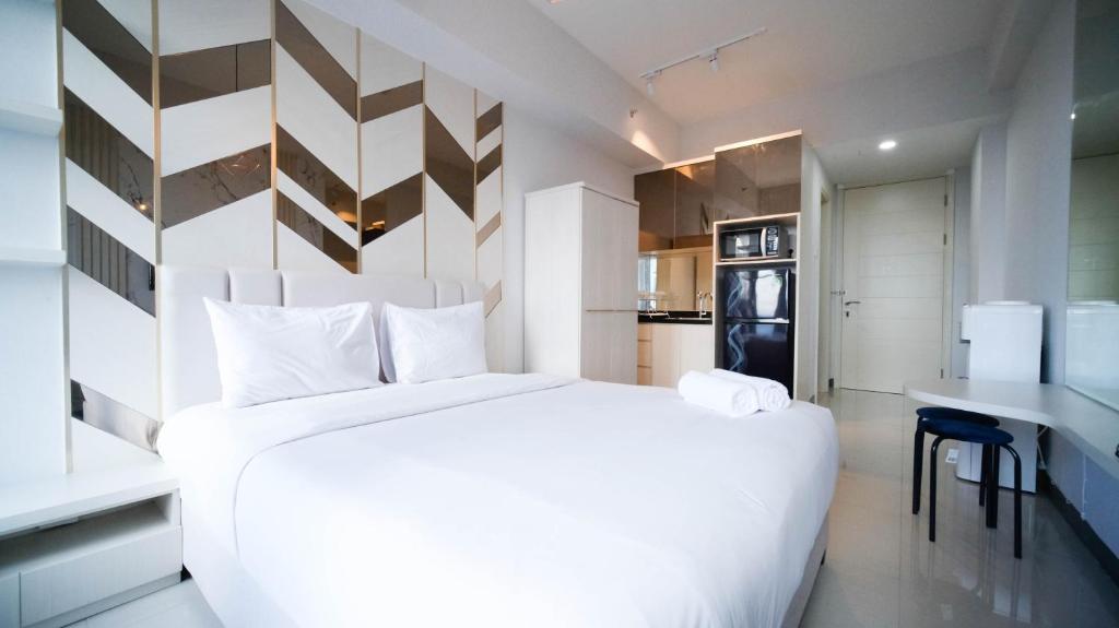 a bedroom with a large white bed and a kitchen at Comfy Studio (No Kitchen) Apartment at Benson Supermall Mansion By Travelio in Surabaya