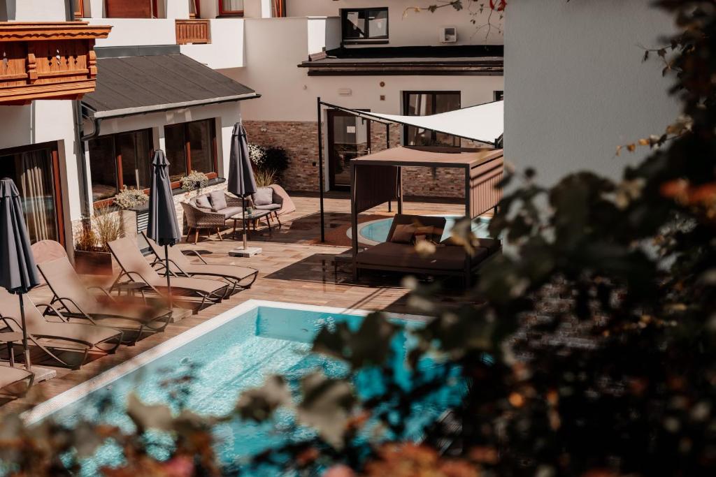 a patio with a swimming pool and chairs and umbrellas at Kinderhotel Laderhof in Ladis
