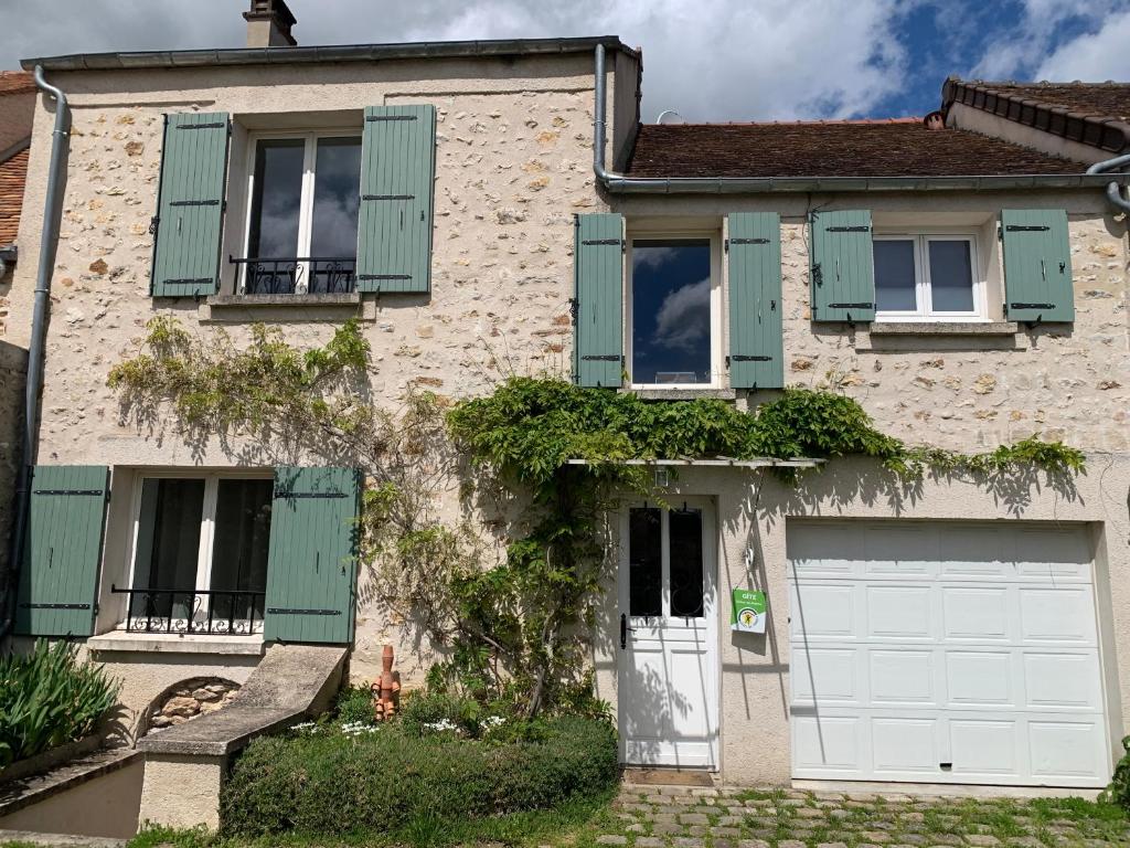 a white house with green shutters and a garage at La Maison Gabriac in Boissise-la-Bertrand
