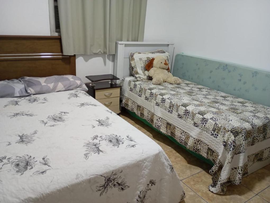 a bedroom with two beds and a teddy bear sitting on a bench at Casa de praia a 100 metros da praia in Passo de Torres