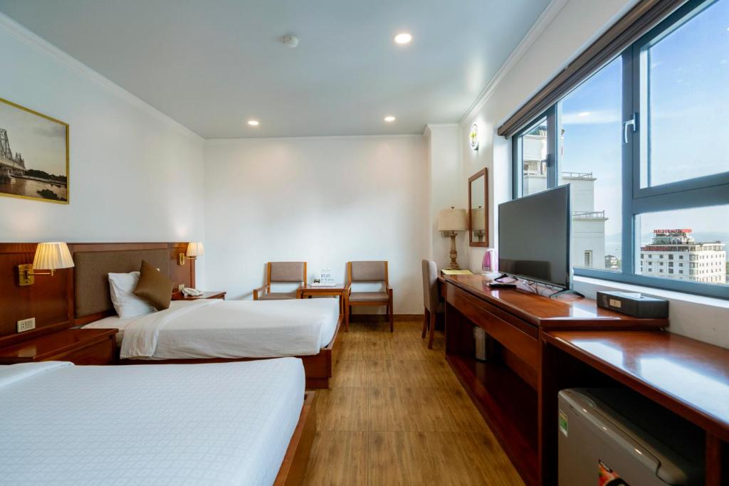 a hotel room with two beds and a desk with a tv at Au Lac Ha Long Hotel in Ha Long