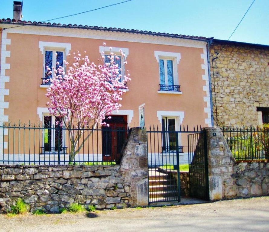 ein Haus mit einem Zaun und einem Baum mit rosa Blumen in der Unterkunft Au Petit Verger in Puivert