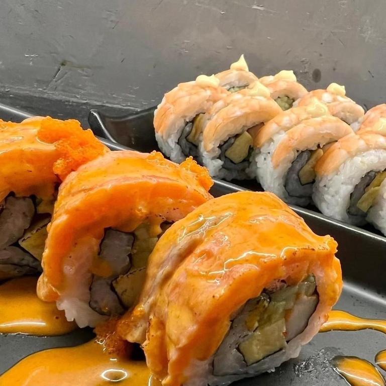 A buffet tray of sushi rolls, including salmon-topped rolls and shrimp rolls.