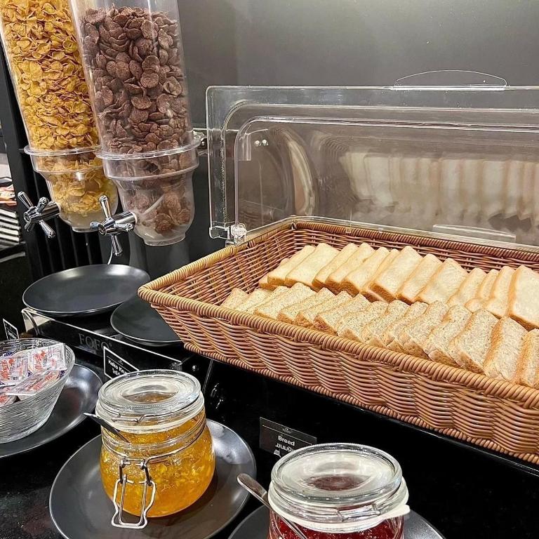 A buffet bread station with cereal dispensers and jars of spreads.
