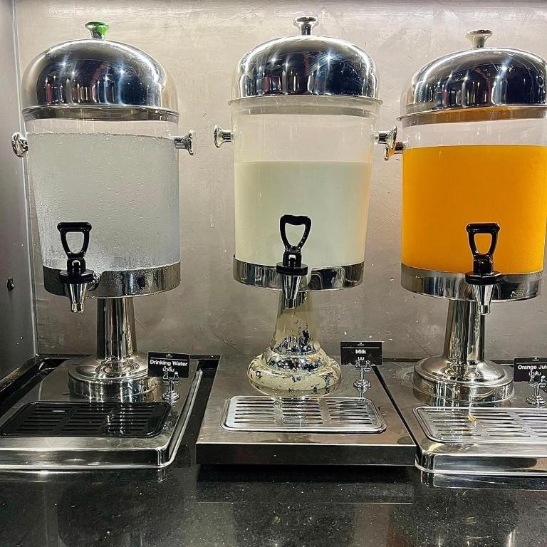 A self-service drinks station with water, milk and orange juice dispensers.