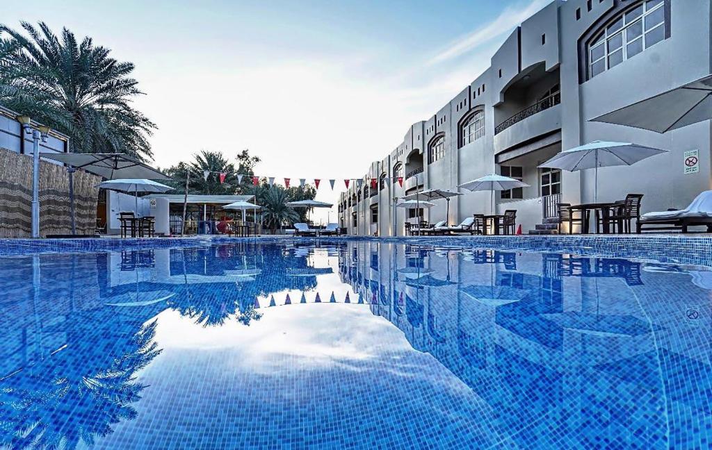 a large swimming pool next to a building with umbrellas at Asfar Resorts Al Ain in Al Ain
