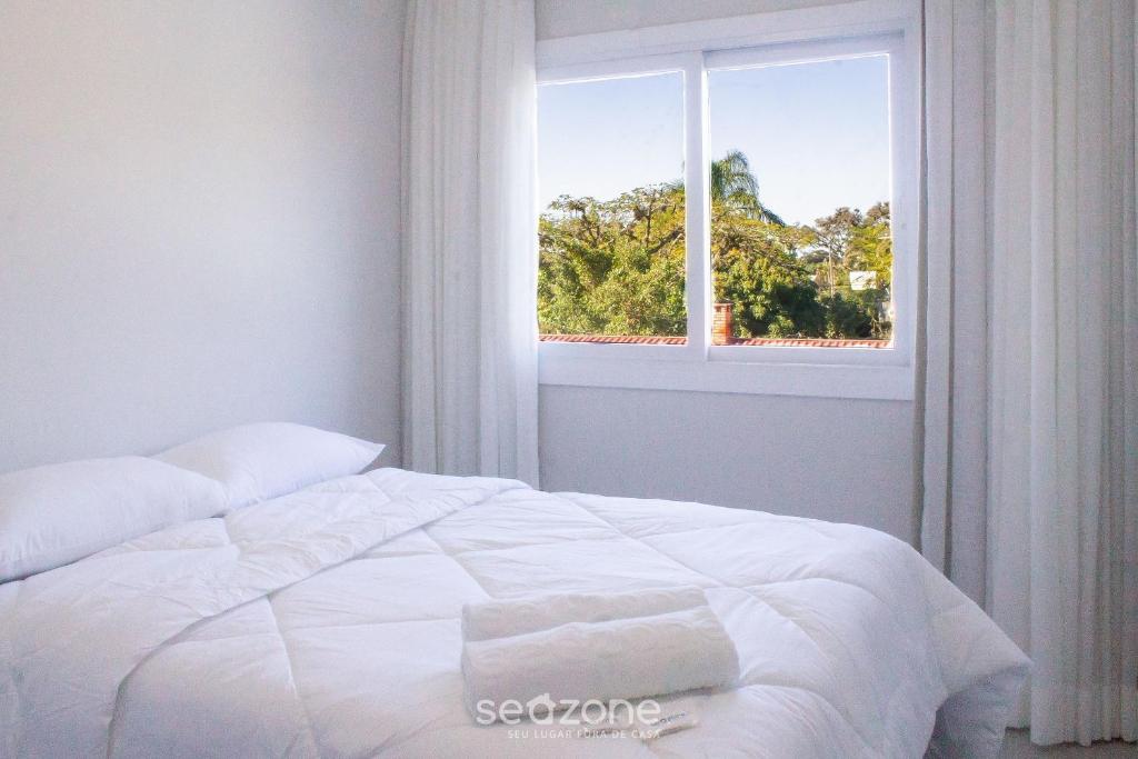 a bedroom with a white bed and a window at Modern apartment with barbecue CRR201 in Florianópolis