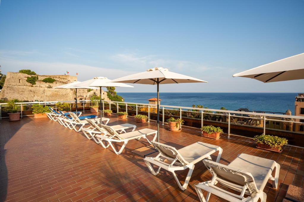 een rij stoelen en parasols op een terras met de oceaan bij Hotel Careni Villa Italia in Finale Ligure