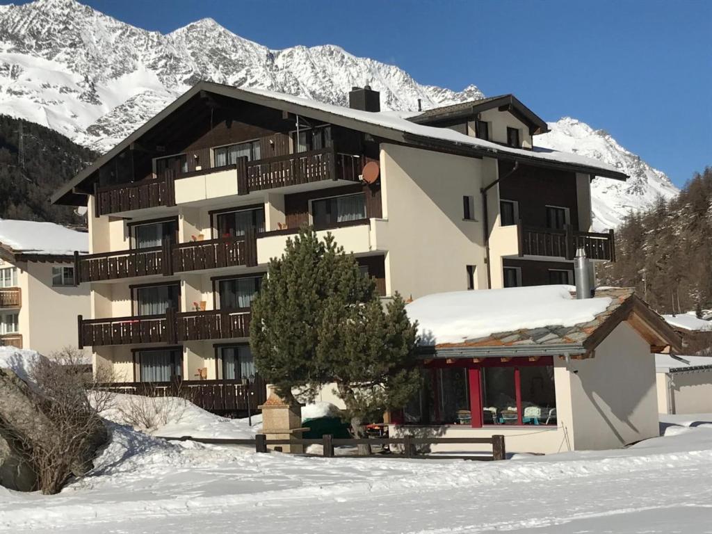 un bâtiment sous la neige avec des montagnes en arrière-plan dans l'établissement Apartment Haus Azur by Interhome, à Saas-Almagell