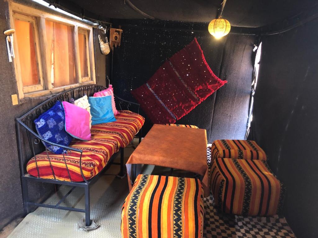 Cette chambre comprend un banc, une table et des oreillers. dans l'établissement Bivouac Le Petit Prince Merzouga, à Merzouga