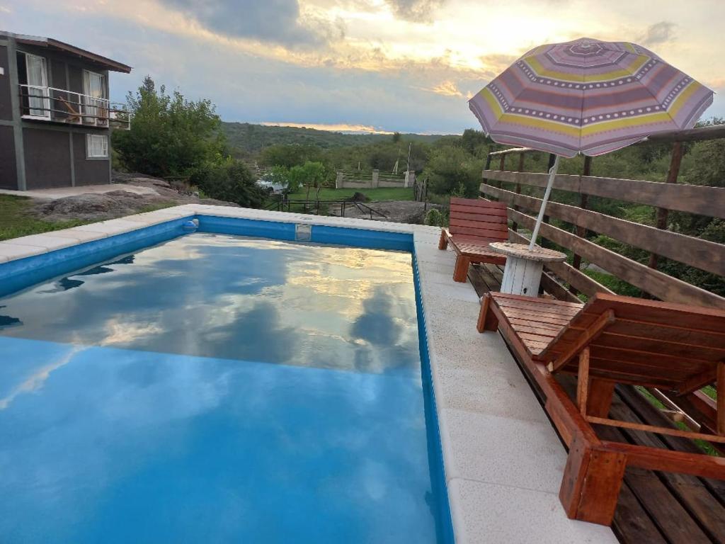 a swimming pool with an umbrella and two benches at Complejo DYE in Bialet Massé