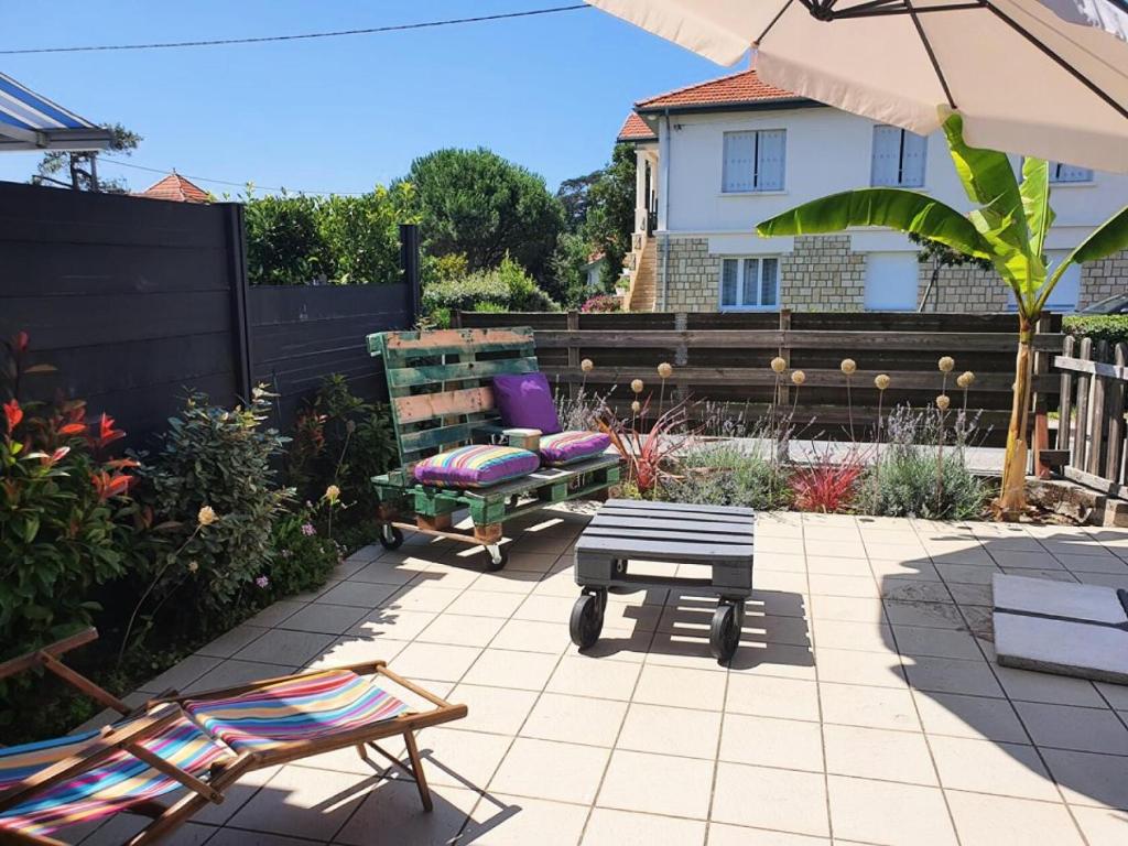 une terrasse avec un banc, une chaise et un parasol dans l'établissement Résidence 042-soulac Sur Mer - 042 - Charmante maison de vacances à Soulac-sur-Mer, à deux pas de la plage MAE-2321, à Soulac-sur-Mer
