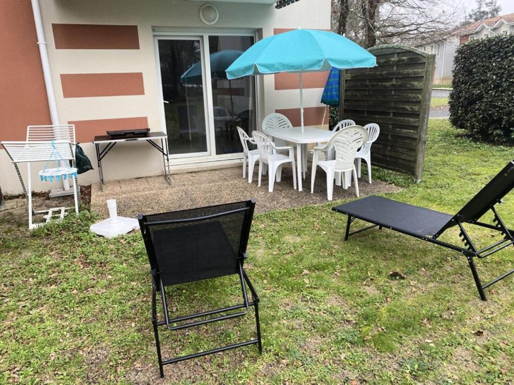 un patio avec une table, des chaises et un parasol dans l'établissement Résidence Domaine Des Sables - 036 - Maison mitoyenne dans un domaine de vacances avec piscine MAE-3581, à Soulac-sur-Mer