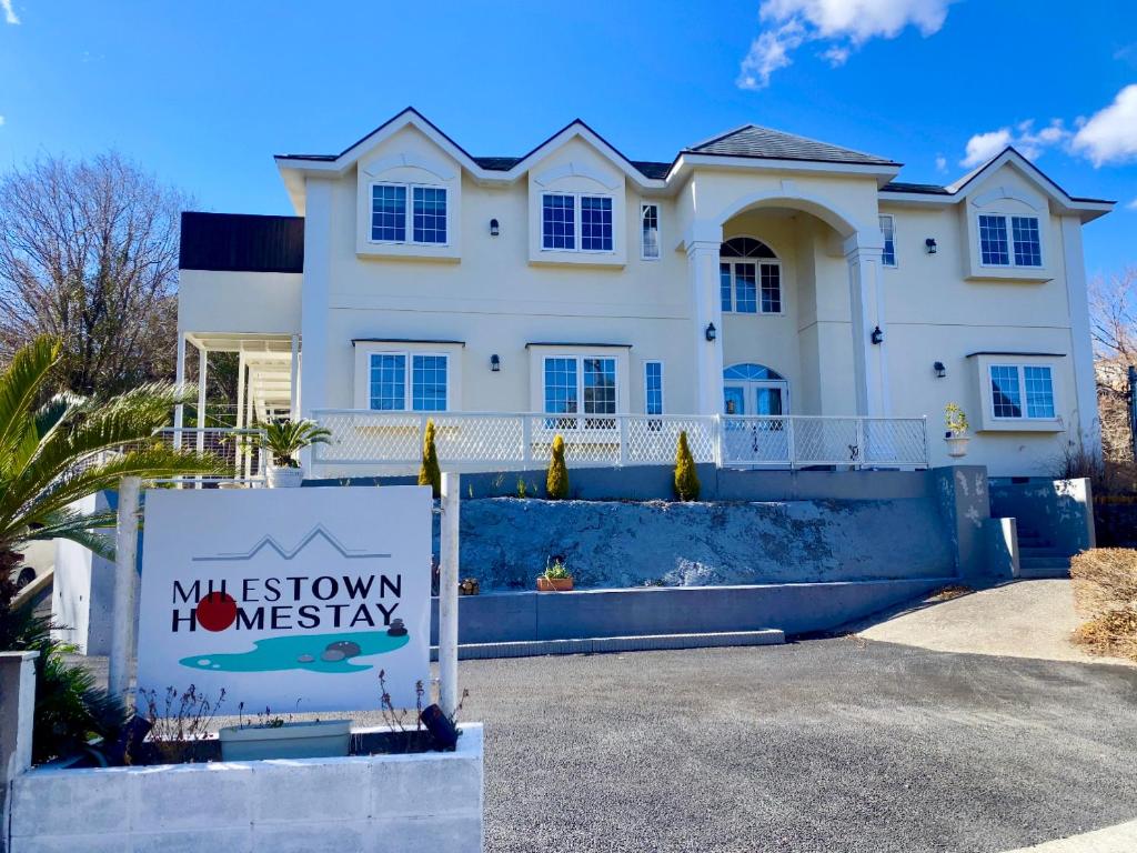 une maison blanche avec un panneau devant dans l'établissement Miles Town, à Itō