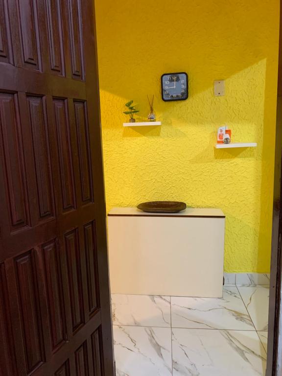 a bathroom with a yellow wall with a clock on the wall at Aconchego Bertioga in Bertioga