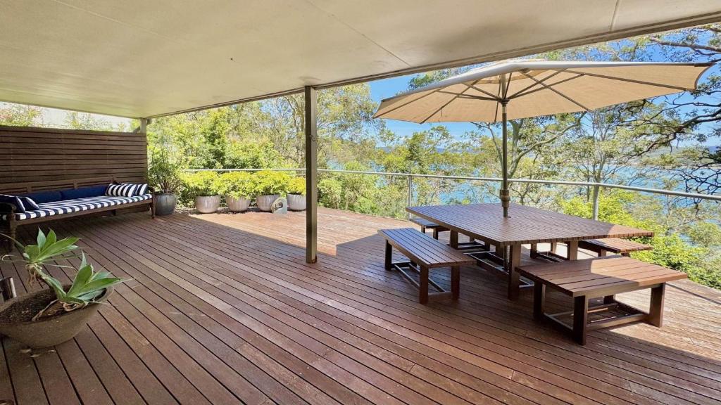 a deck with a table and benches and an umbrella at 'Pretty Beach Escape' by HolidayCo in Pretty Beach