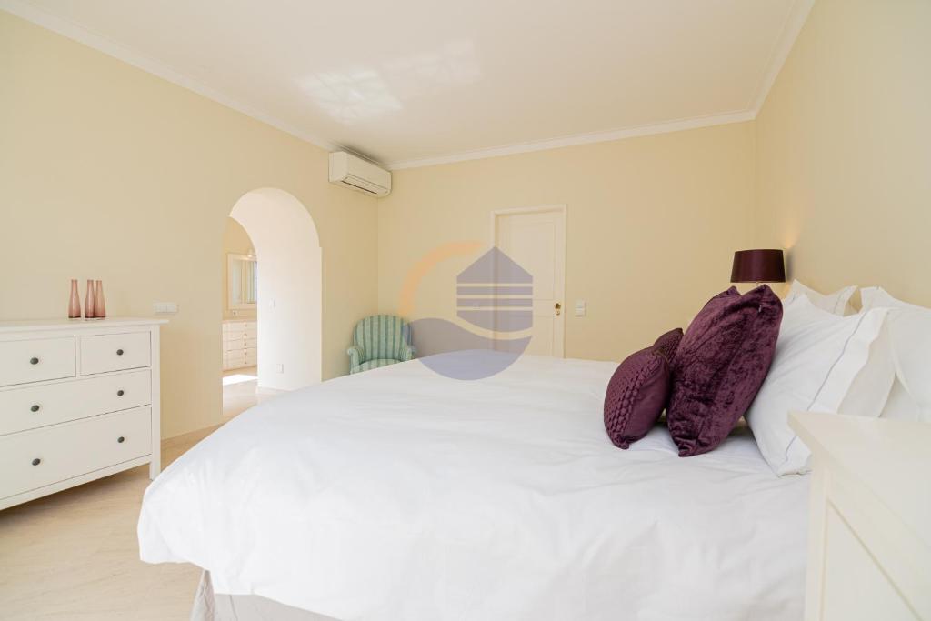ein Schlafzimmer mit einem weißen Bett mit lila Kissen in der Unterkunft Villa Suites Outdoor pool with golf view in Portimão
