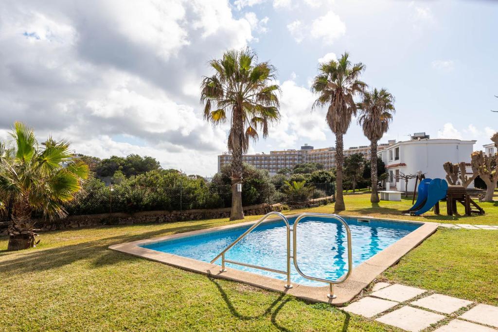 a pool with a slide in a yard with palm trees at Menorca Apartamento ALOHA by Mauter Villas in Cala en Blanes