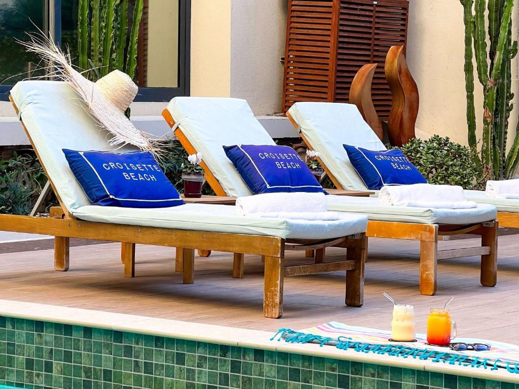 two lounge chairs with blue pillows sitting next to a pool at Croisette Beach Hotel Cannes - MGallery Collection in Cannes