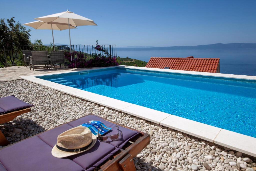 a swimming pool with a hat sitting on a bench next to it at Wunderschöne Steinvilla Mit Tollem Ausblick in Podgora