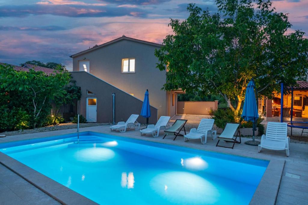 a swimming pool with chairs and umbrellas in front of a house at Ferienhaus Leone in Bibići