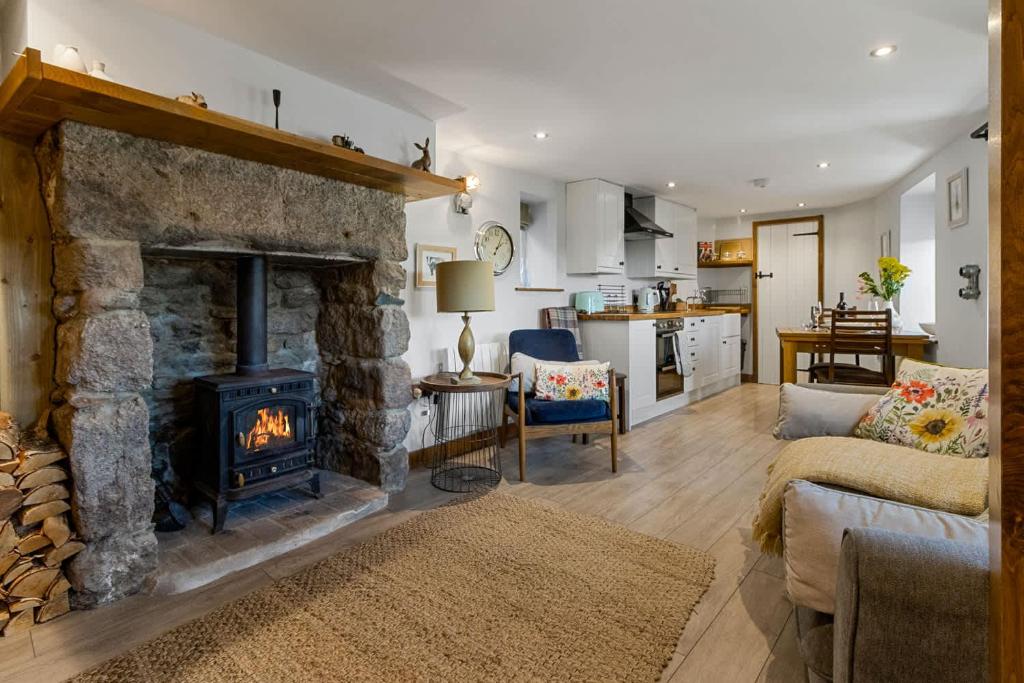 a living room with a stone fireplace and a kitchen at Angler's Cottage - Short Stays UK Ltd in Bridford