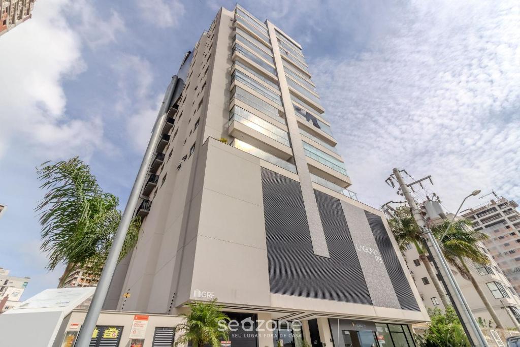 a tall white building with palm trees in front of it at Desfrute do melhor de Perequê a 150m do mar! CLE in Perequê