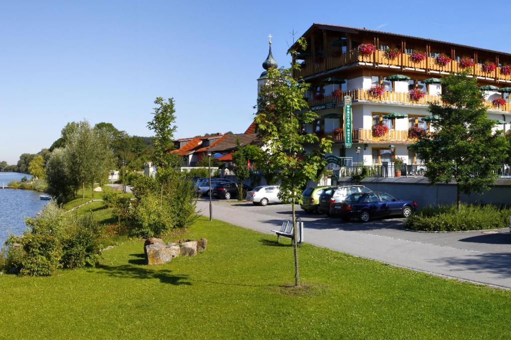 a building with cars parked in a parking lot next to a river at Hotel Restaurant Zum Goldenen Anker mit Hallenbad in Windorf